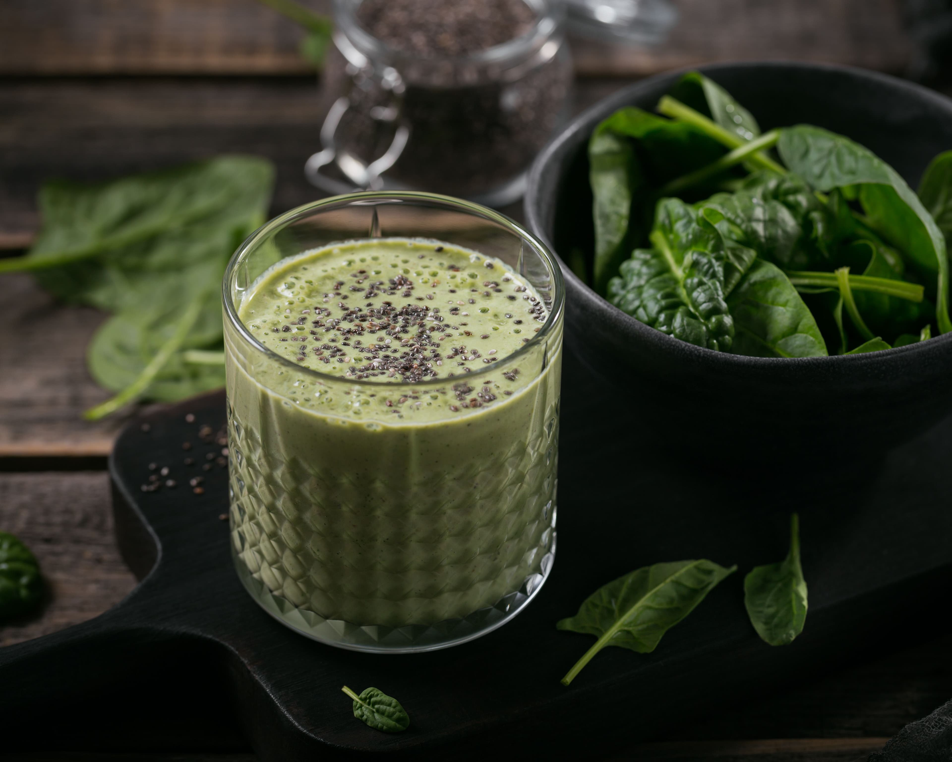 Healthy green smoothie made with fresh spinach served in a clear glass on a rustic wooden surface.