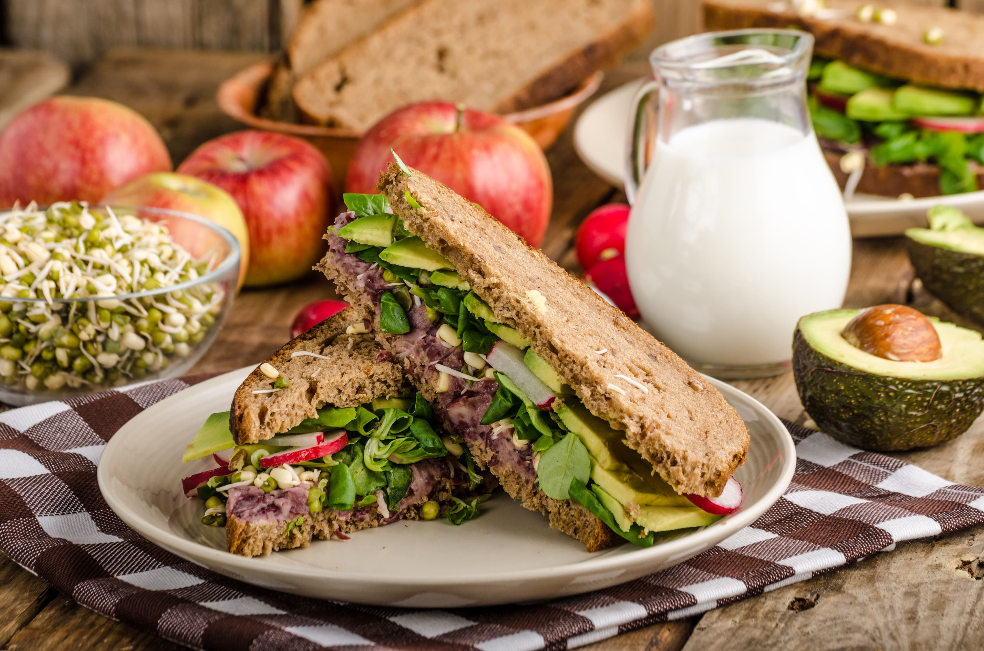 Gluten-free sandwich filled with fresh vegetables like avocado, radish, sprouts, and greens, made with dairy-free and gluten-free bread, served on a rustic plate for a clean and healthy lunch.