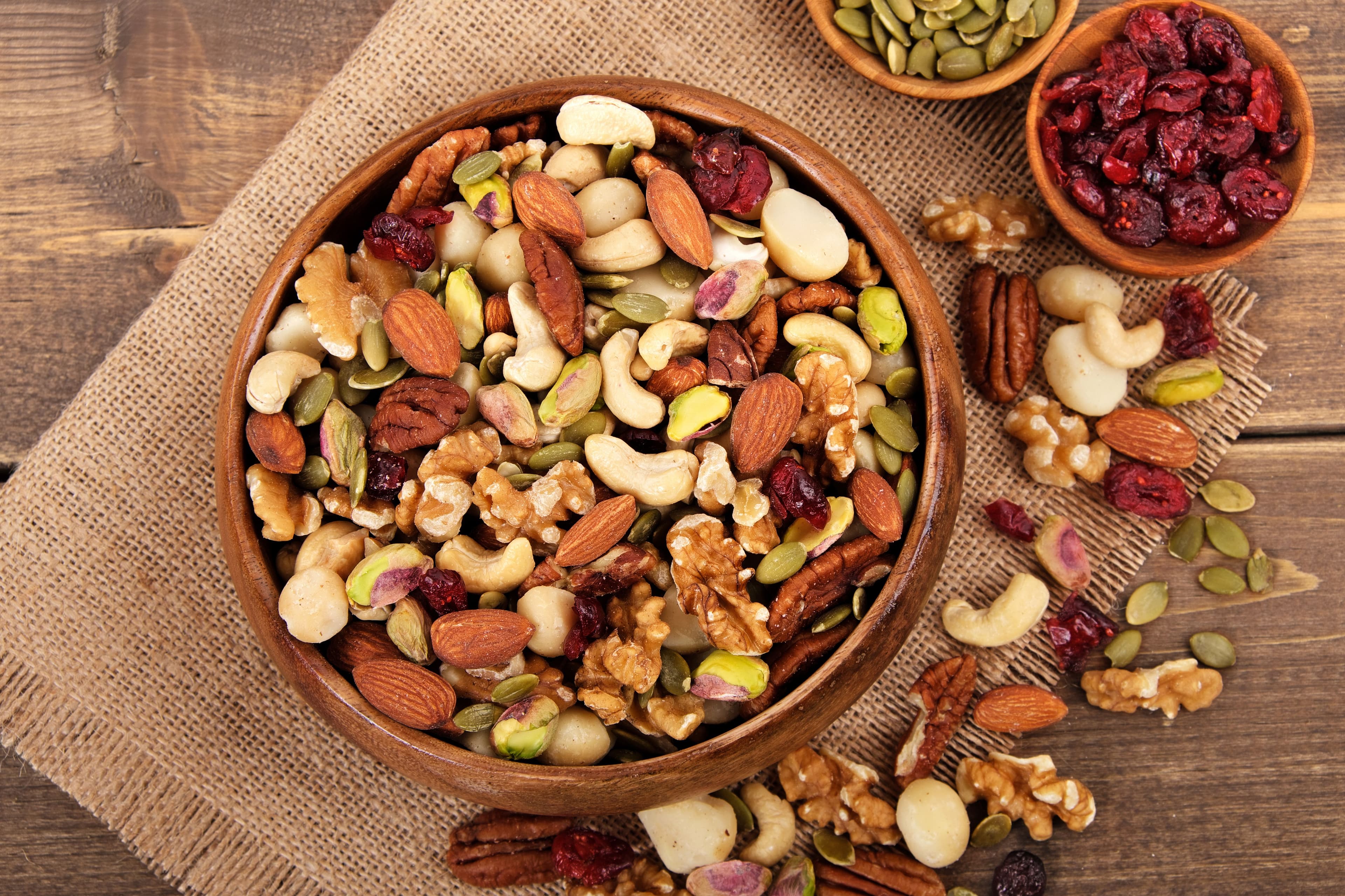 Assorted mixed nuts in a wooden bowl with pumpkin seeds, almonds, walnuts, and dried cranberries