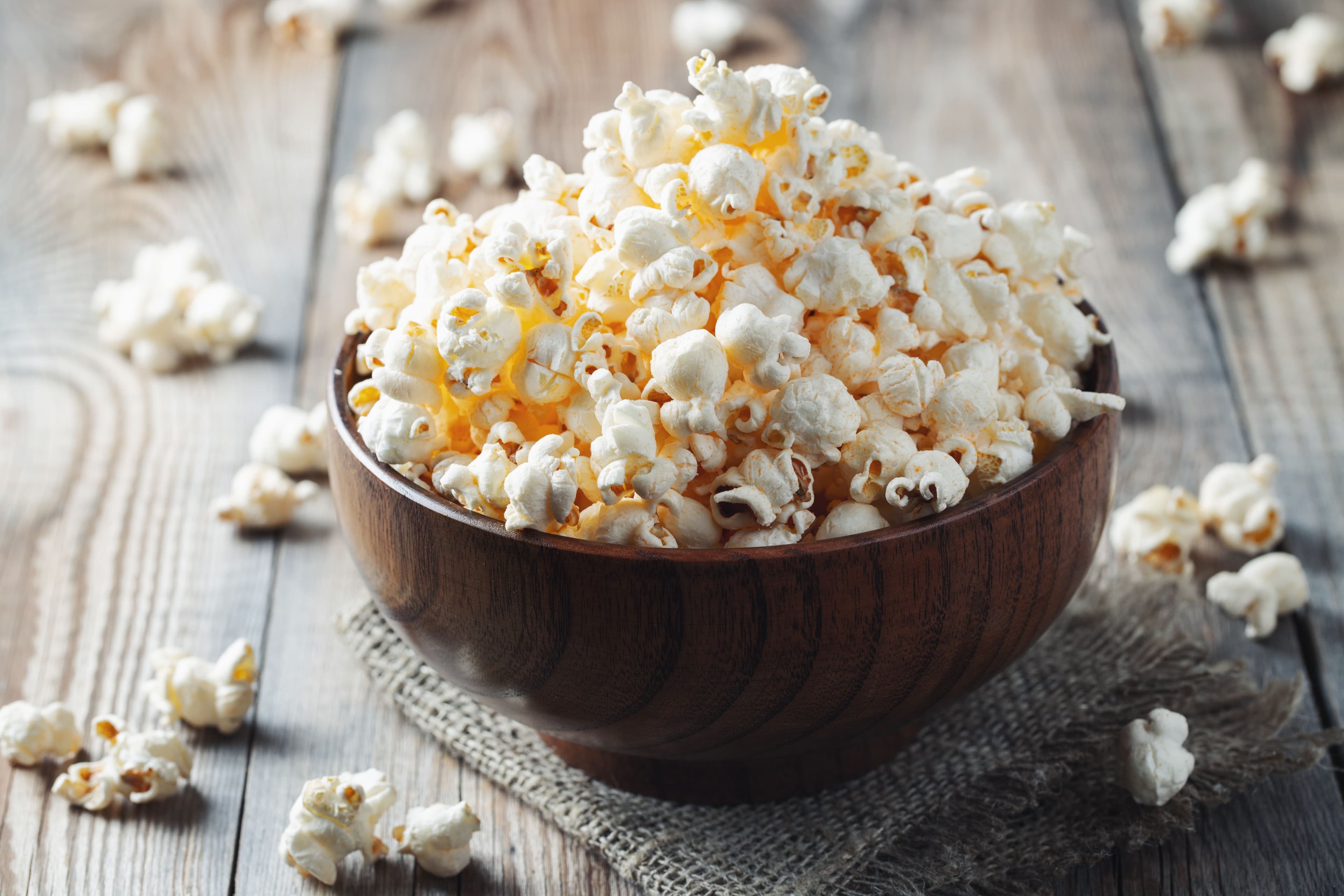 A wooden bowl filled with lightly salted popcorn on a rustic wooden table, a smart and simple healthy snack.