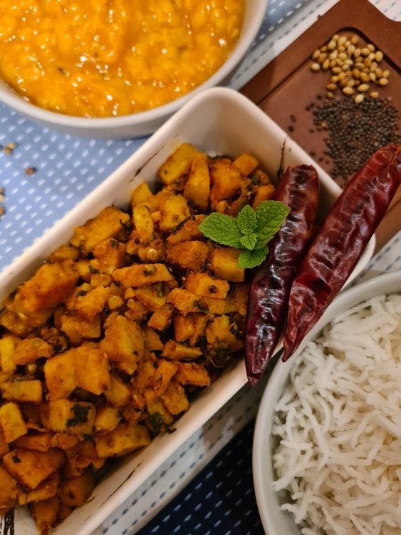 Jeera Aloo (Spiced Cumin Potatoes) in a white bowl next to a bowl of lentils and rice. 