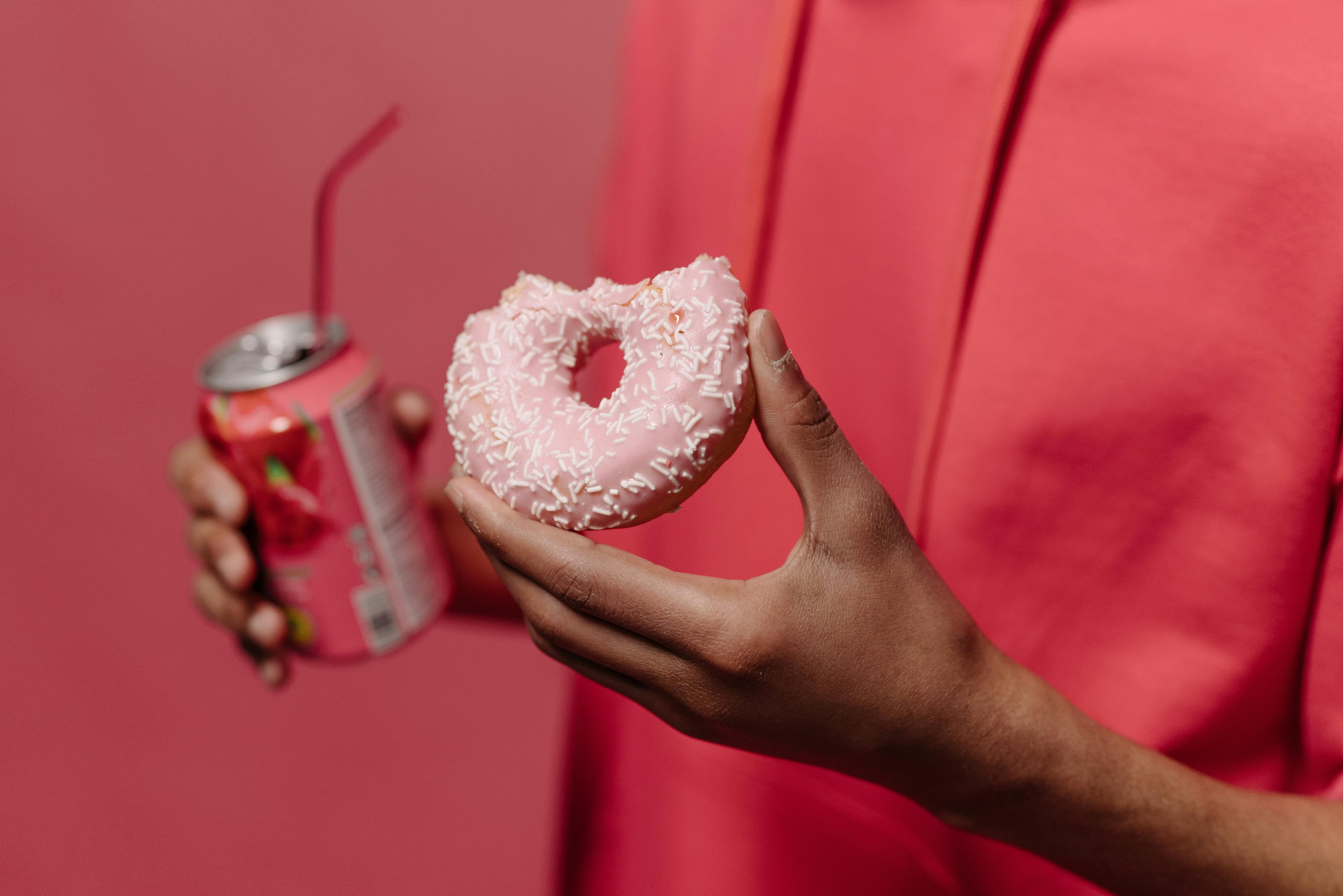 A person holding half eaten donut and a sugary soda