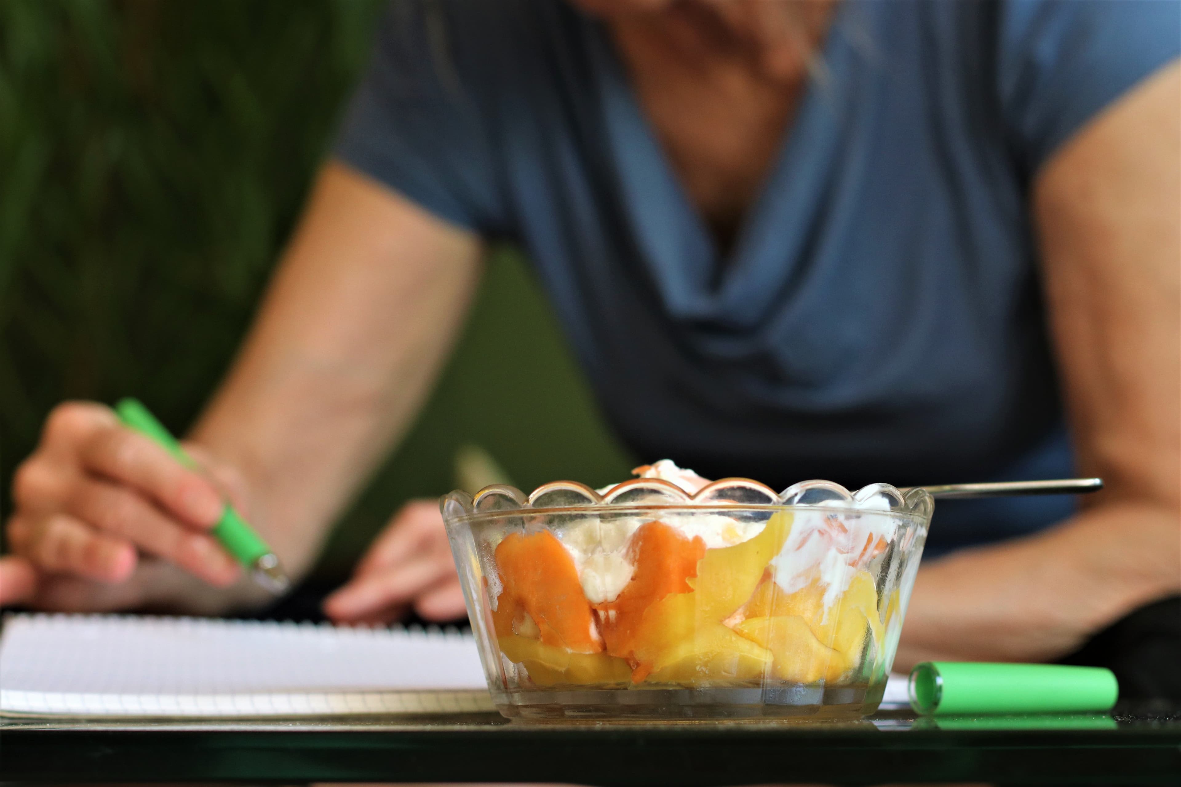 Woman writing a dessert recipe in a notebook with ingredients in the kitchen.