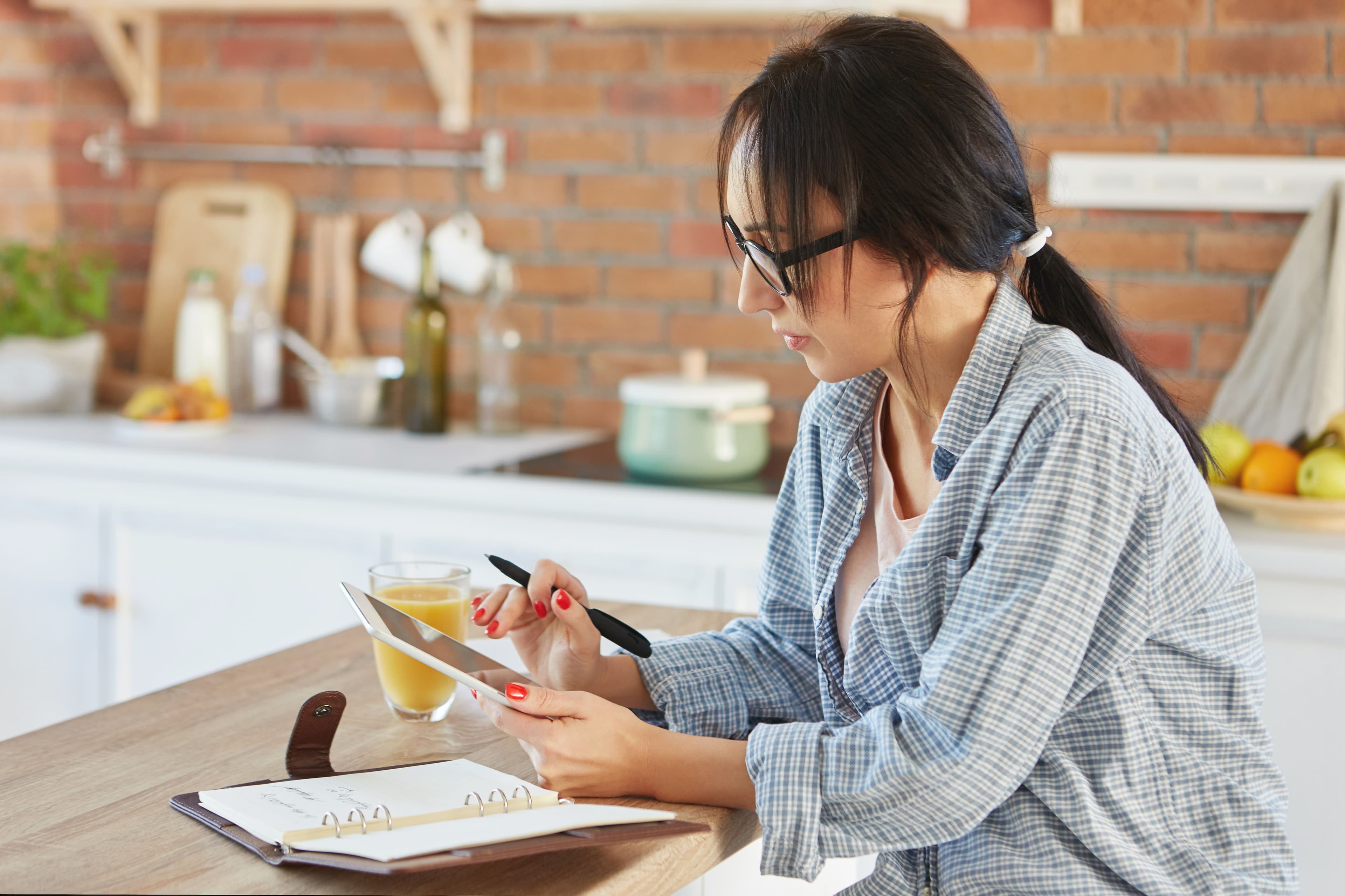 A woman drafting a recipe on a tablet with a notebook beside her, representing the thoughtful process behind recipe writing.
