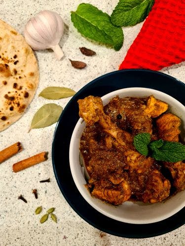 Chicken curry in a bowl surrounded by spices and roti. 