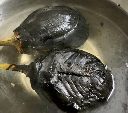 Two roasted eggplants in a bowl of water.