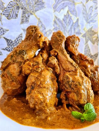 Chicken Drumsticks covered in thick gravy with a sprig of mint on the side