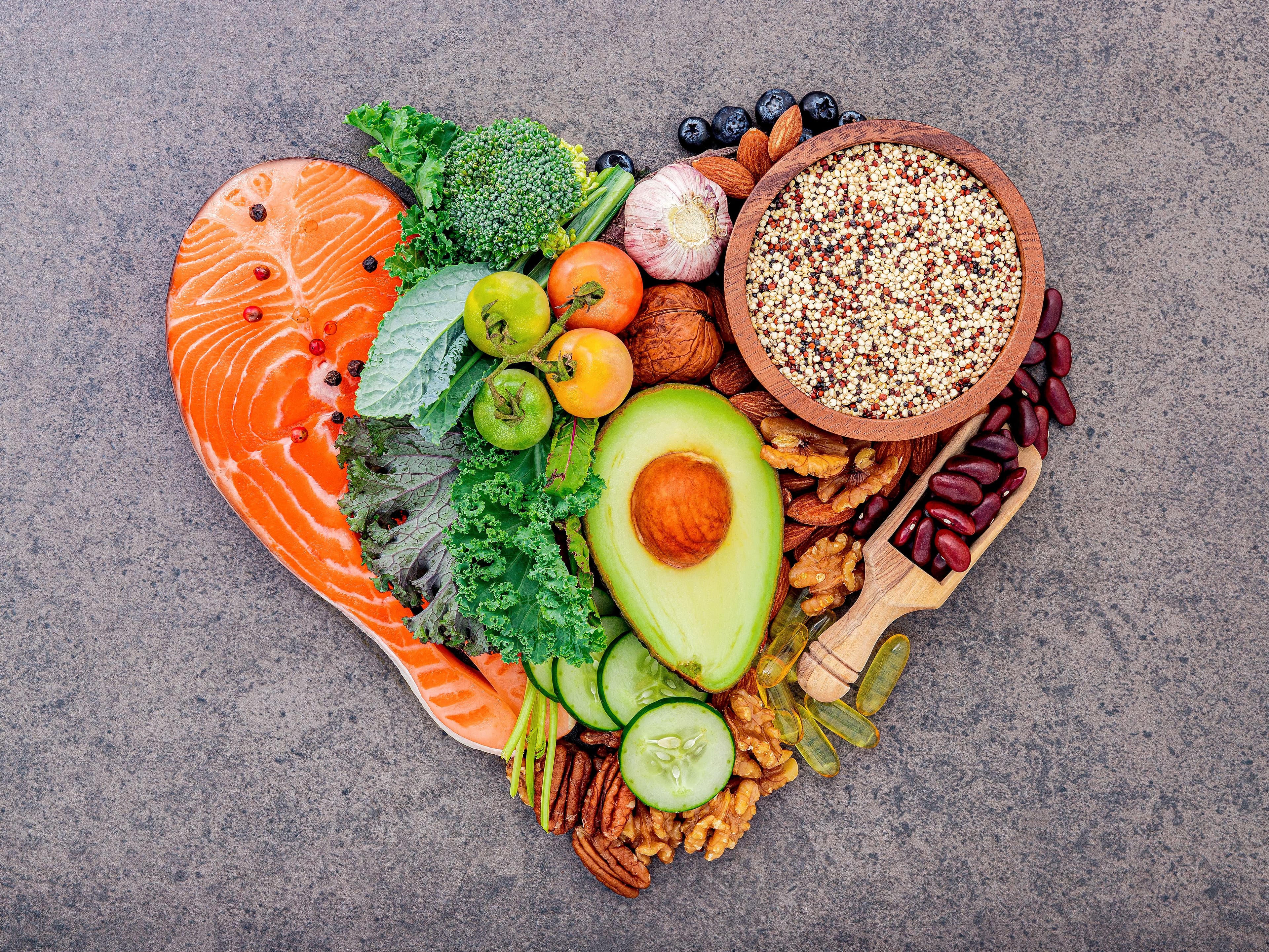 High-angle view of whole food ingredients including salmon, leafy greens, beans, grains, and vegetables for a balanced diet
