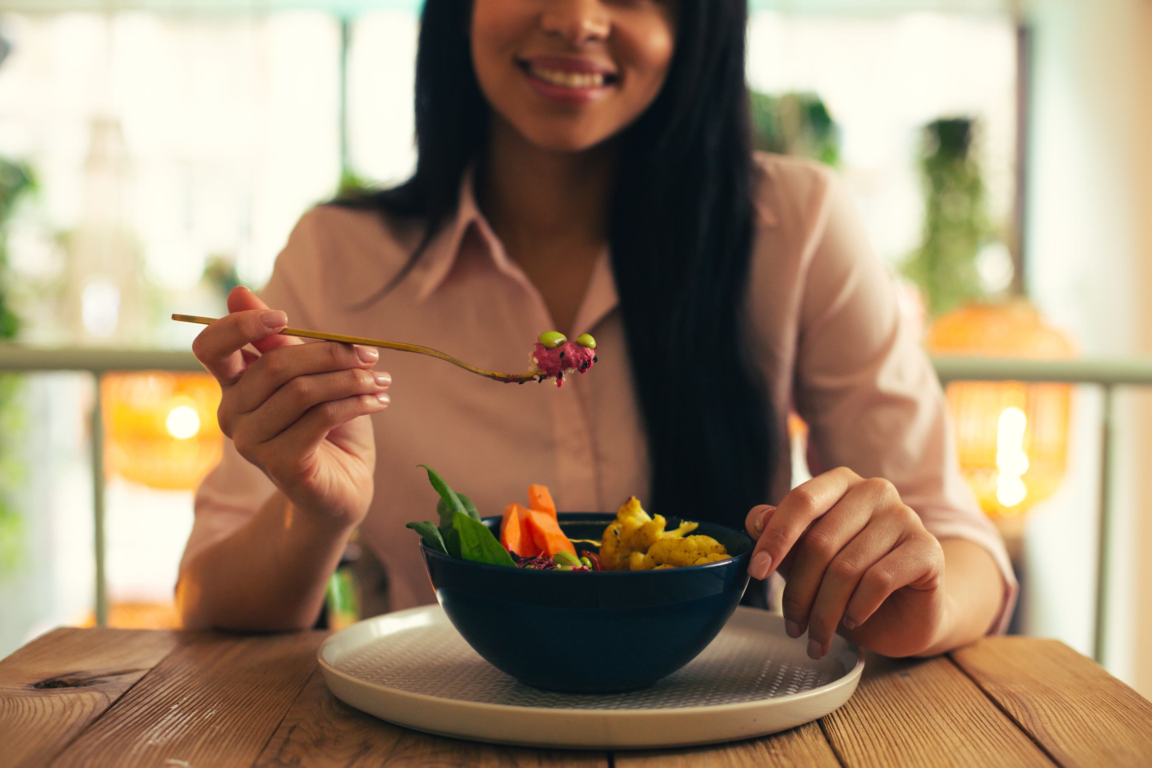Smiling woman holding a fork while enjoying a healthy vegetarian meal, highlighting the joy of healthy snacking.