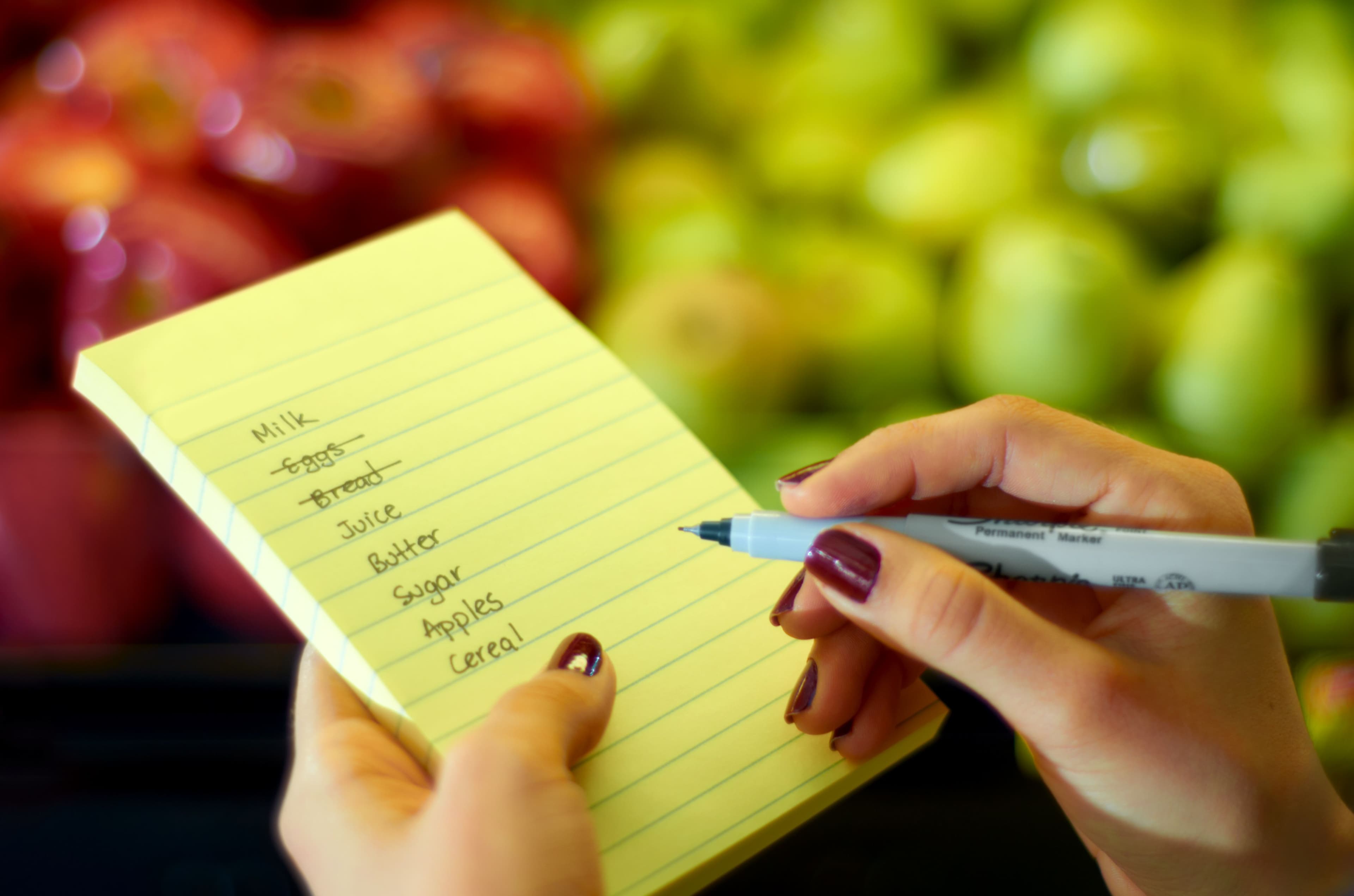 Handwriting a healthy grocery list on a notepad in a supermarket produce aisle