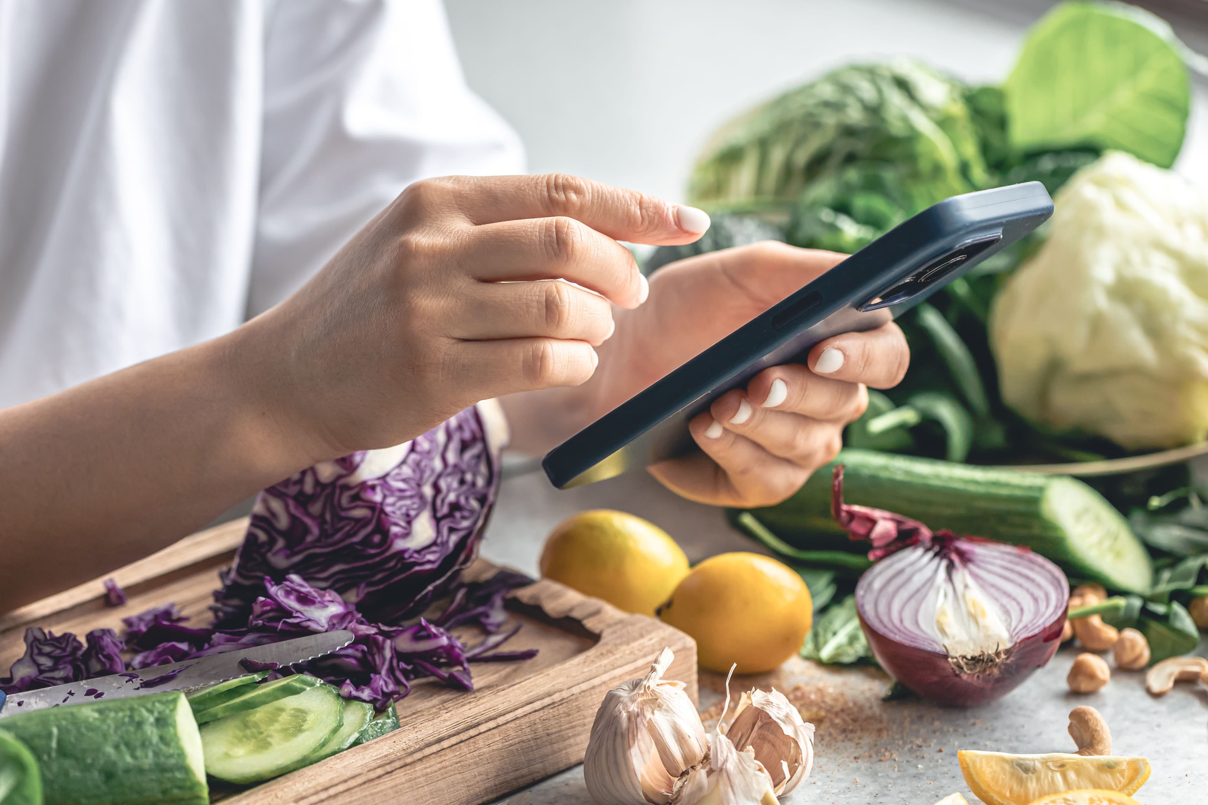 Woman preparing a vegetable salad while using a smartphone in a zero-waste kitchen